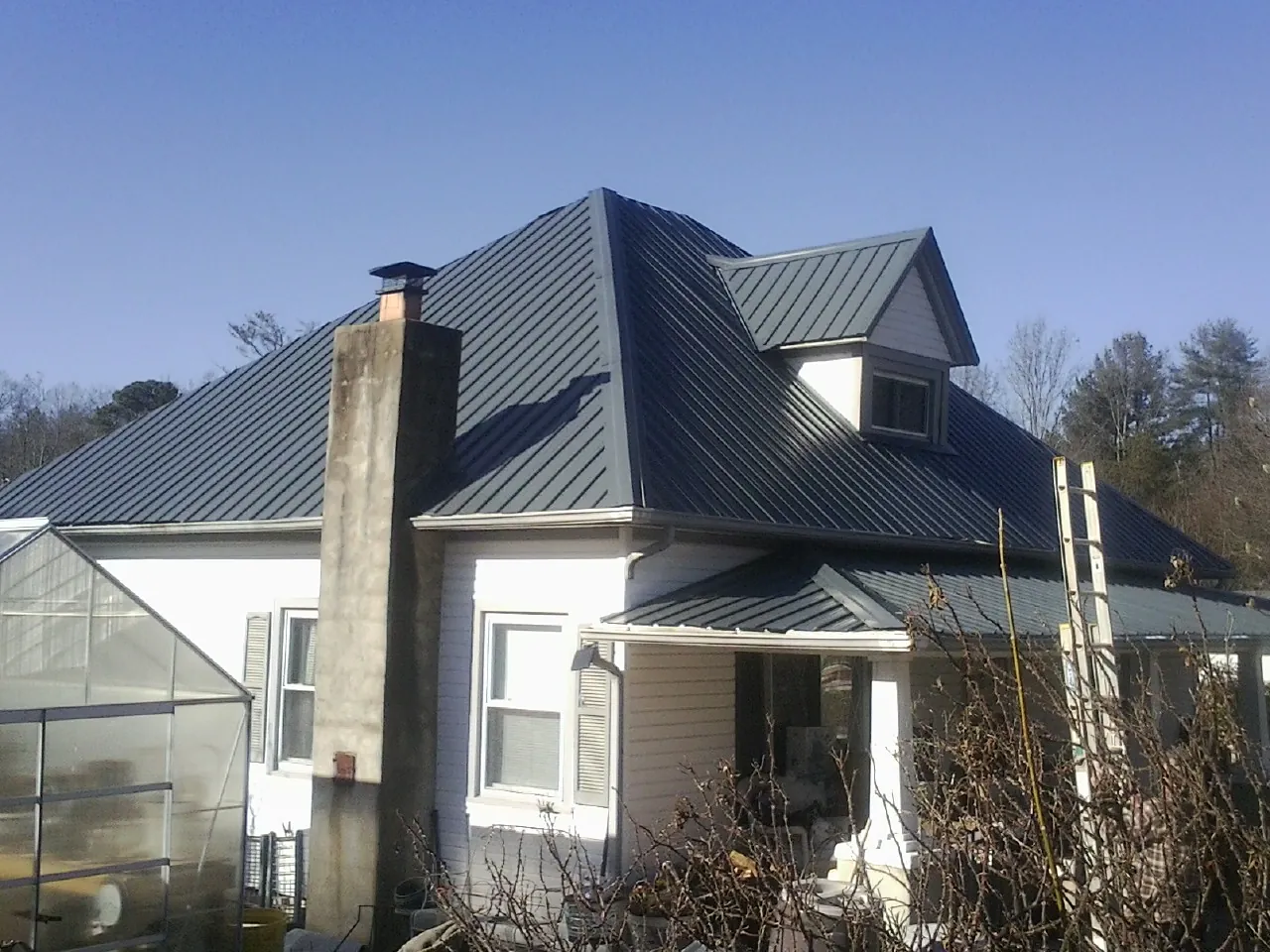 Dark blue standing seam metal roof on a white farmhouse with dormer in Coldspring