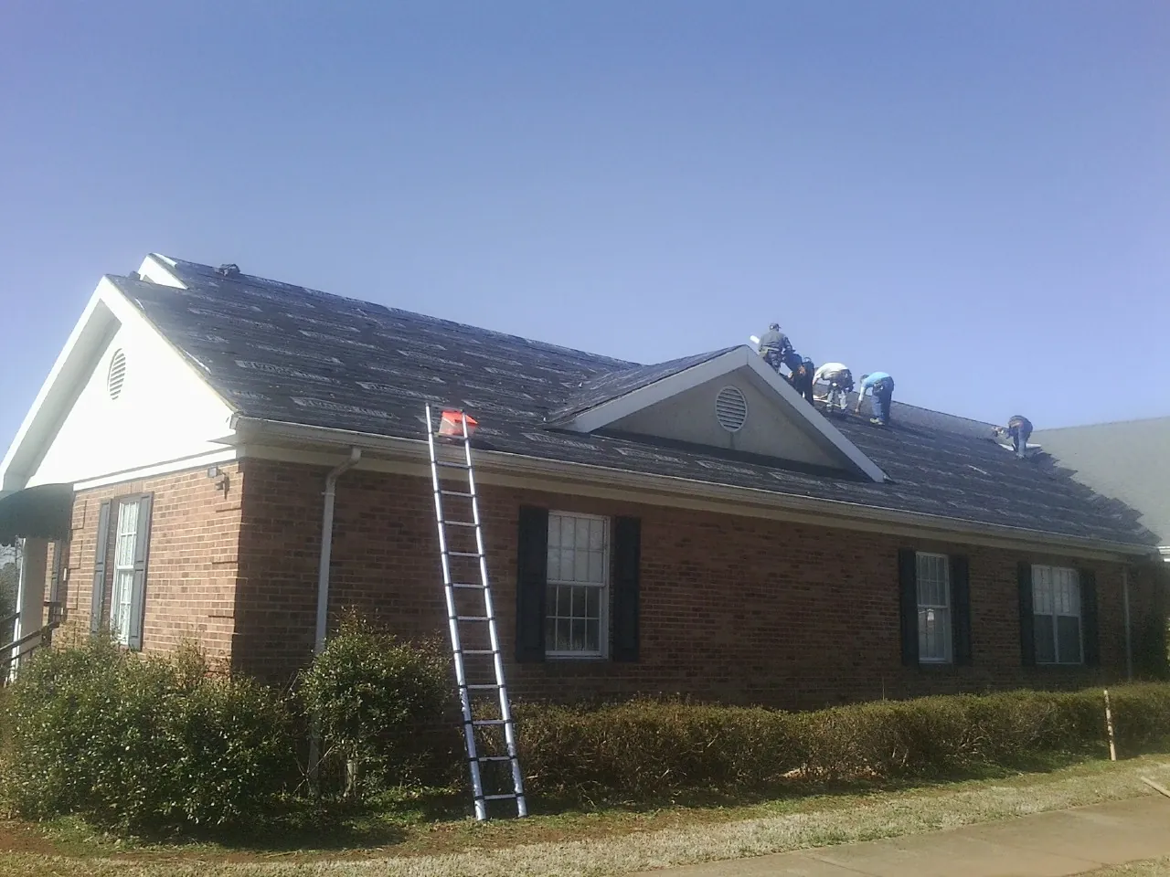 Crew tearing shingles off a brick ranch roof with a ladder set — Emergency Roof Repair work by our crew in Coldspring