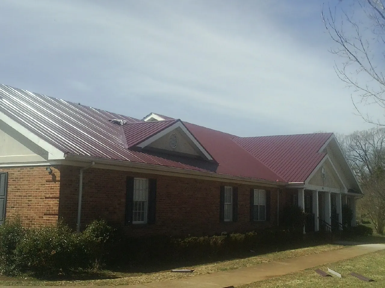 Red metal roof with gabled entries on a long brick building, from a Hail Damage Roof Repair job in Coldspring