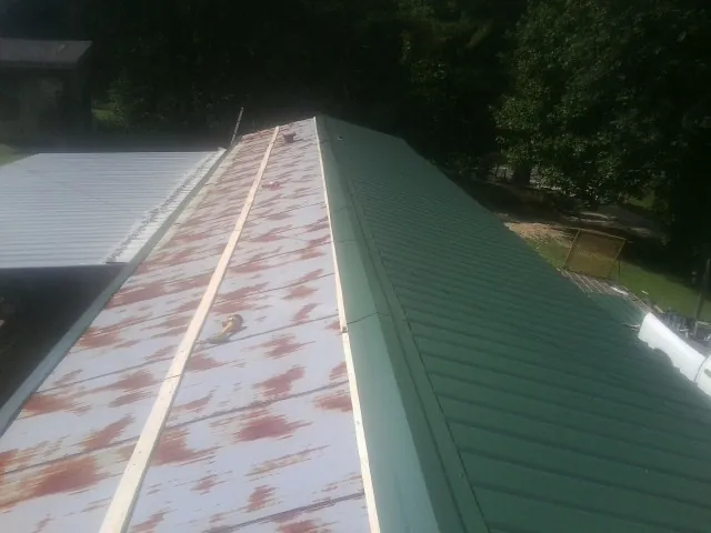 Old rusted panels beside newly installed green metal roofing — Wind Damage Roof Repair by Roofing Brothers in Coldspring