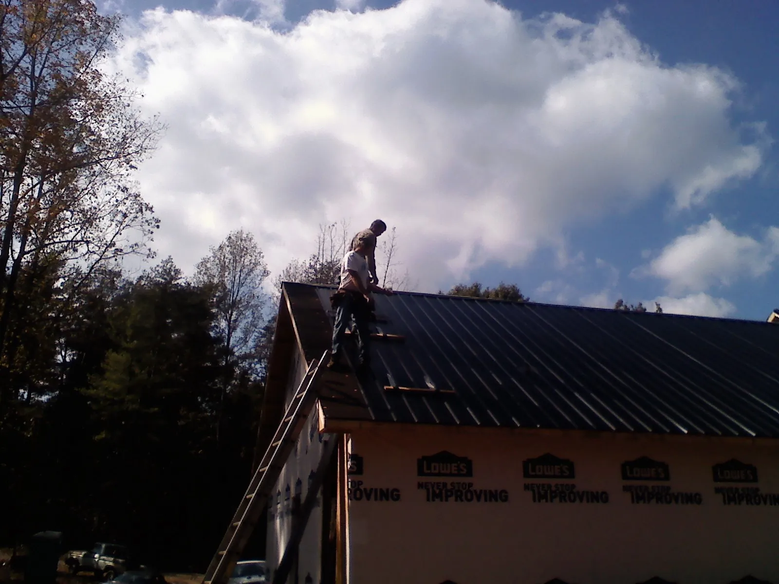Roofer fastening dark metal panels high against a cloudy sky, from a Roof Inspection job in Coldspring