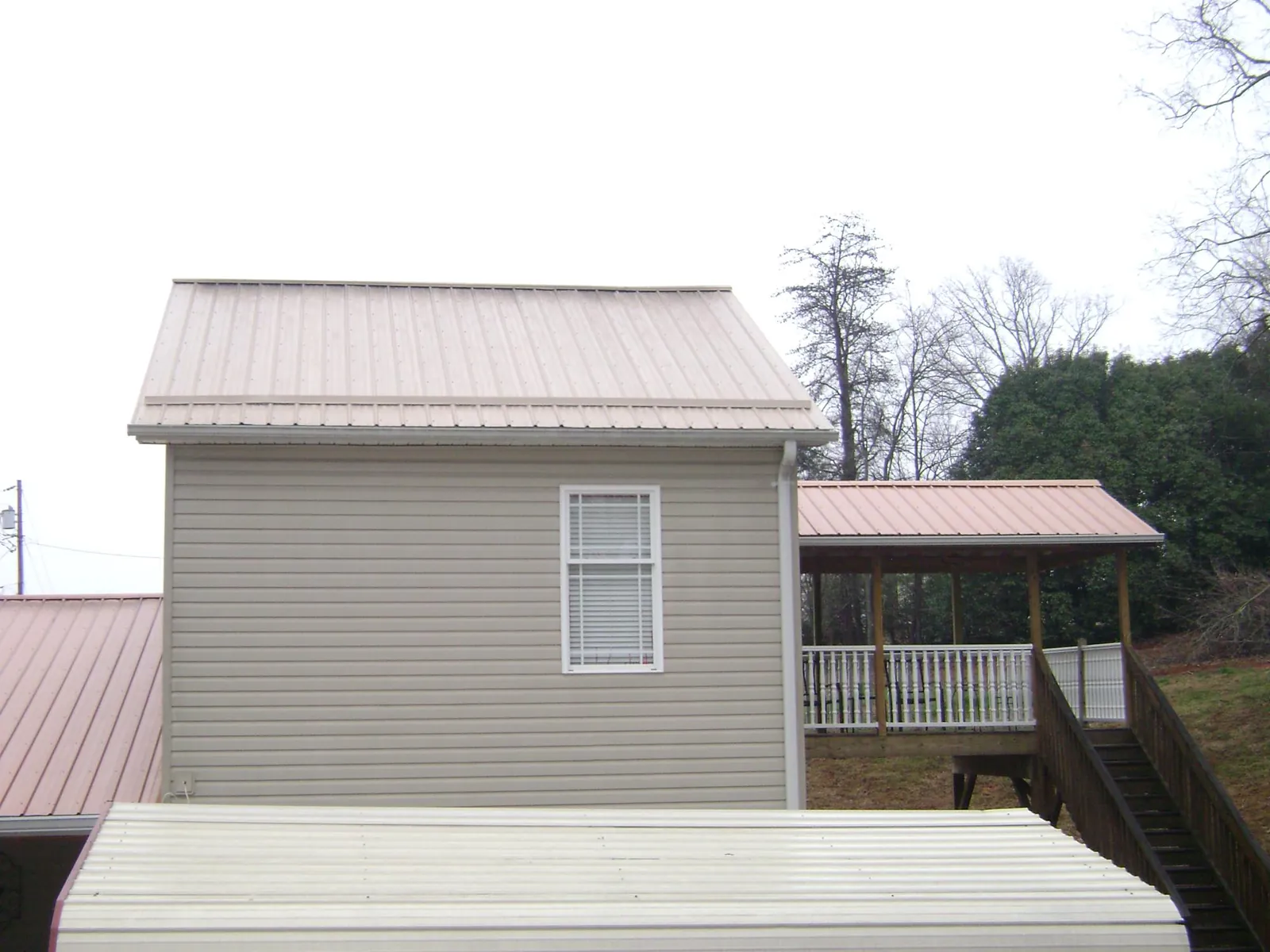 Tan metal roofs on a two story addition and attached porch, from a Roof Replacement job in Coldspring